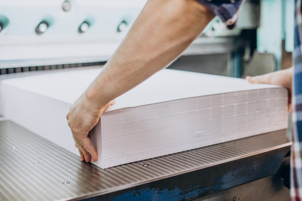 Hand lägger en tjock bunt vitt papper på bordet i en pappersskärmaskin